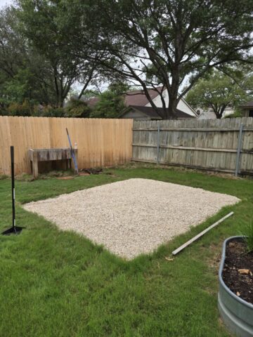 Grassy suburban backyard with an area filled with gravel to create a level area to build some raised bed gardens.