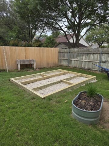 Suburban backyard with a level gravel pad and treated lumber foundation for some raised bed gardens.