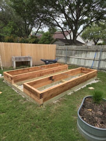 Suburban backyard with a level gravel pad, treated lumber foundation, and the beginning stages of building cedar raised garden beds.