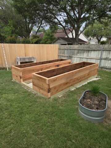 Suburban backyard with a level gravel pad, treated lumber foundation, and cedar raised garden beds now at finished height..